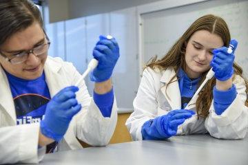 Students Nathan Rice, 24岁 和 Lexi Lumley, 24岁 conduct research in labcoats 和 blue gloves.