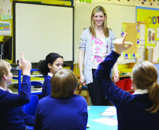 Teacher in a classroom with students raising their h和s.